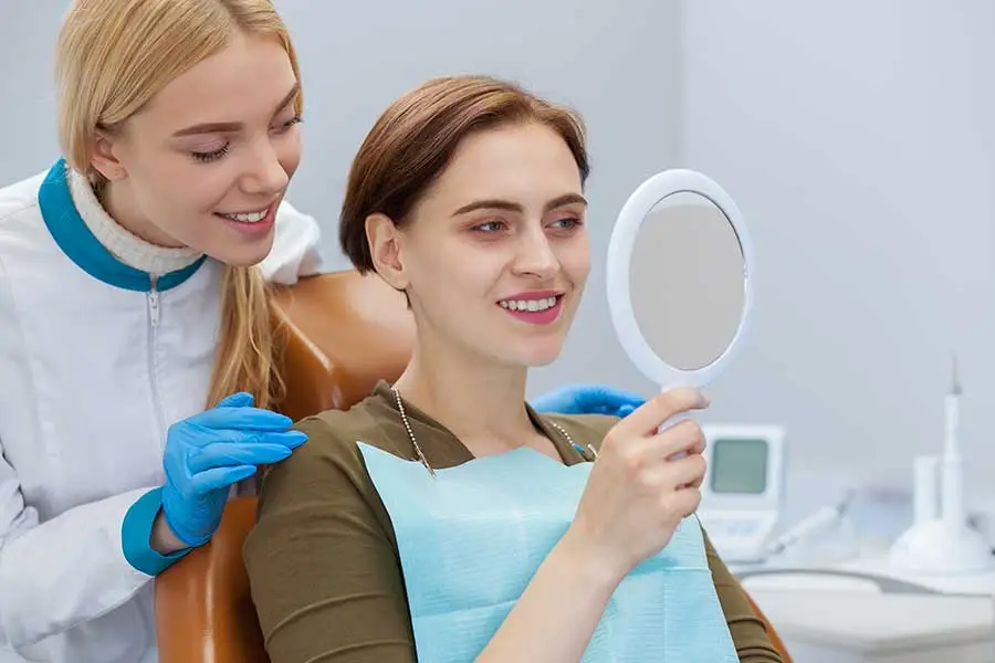 Patient looking in the mirror and checking her teeth at dental office